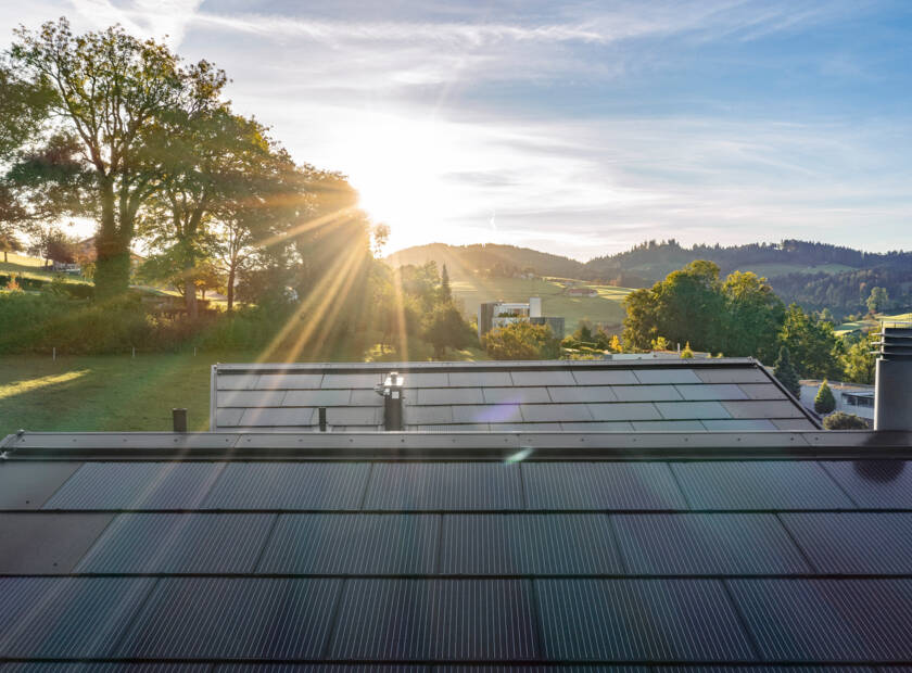Ein modernes Haus mit einem Solardach. Das Haus ist weiss mit einem Schrägdach und grossen Fenstern. Das Dach ist mit dem perfekt integrierte Photovoltaik-Dachsystem Sunskin Roof Lap bedeckt. Das Haus steht auf einem Hügel mit einem grossen Garten und Bäumen. EFH, St. Gallen, CH